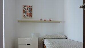 Une chambre à coucher avec un lit, une table de chevet, une lampe, une étagère avec des tasses et une affiche accrochée au mur.