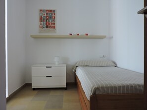 A bedroom with a bed, a nightstand, a lamp, a shelf with cups, and a poster on the wall.