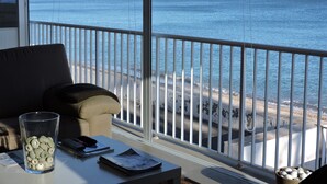 Un balcon avec vue sur la mer et les falaises, une table en verre ornée d’une collection de coquillages et un canapé.