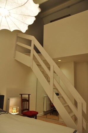 Ein Schlafzimmer mit einer Holztreppe, einer Nachttischlampe und einem roten Sessel.