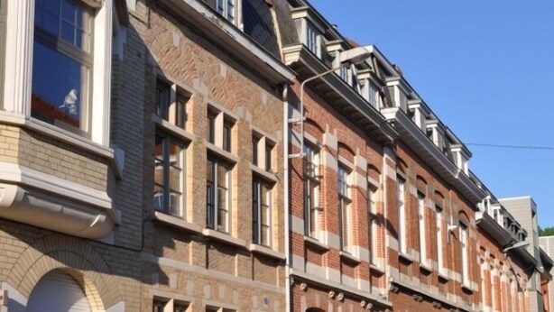 Een rij herenhuisjes van baksteen met gelijkmatige raampatronen en een kinderafsluiting van cobblestones.
