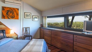 A bedroom with a large window, a bed, a dresser, and artwork on the wall.