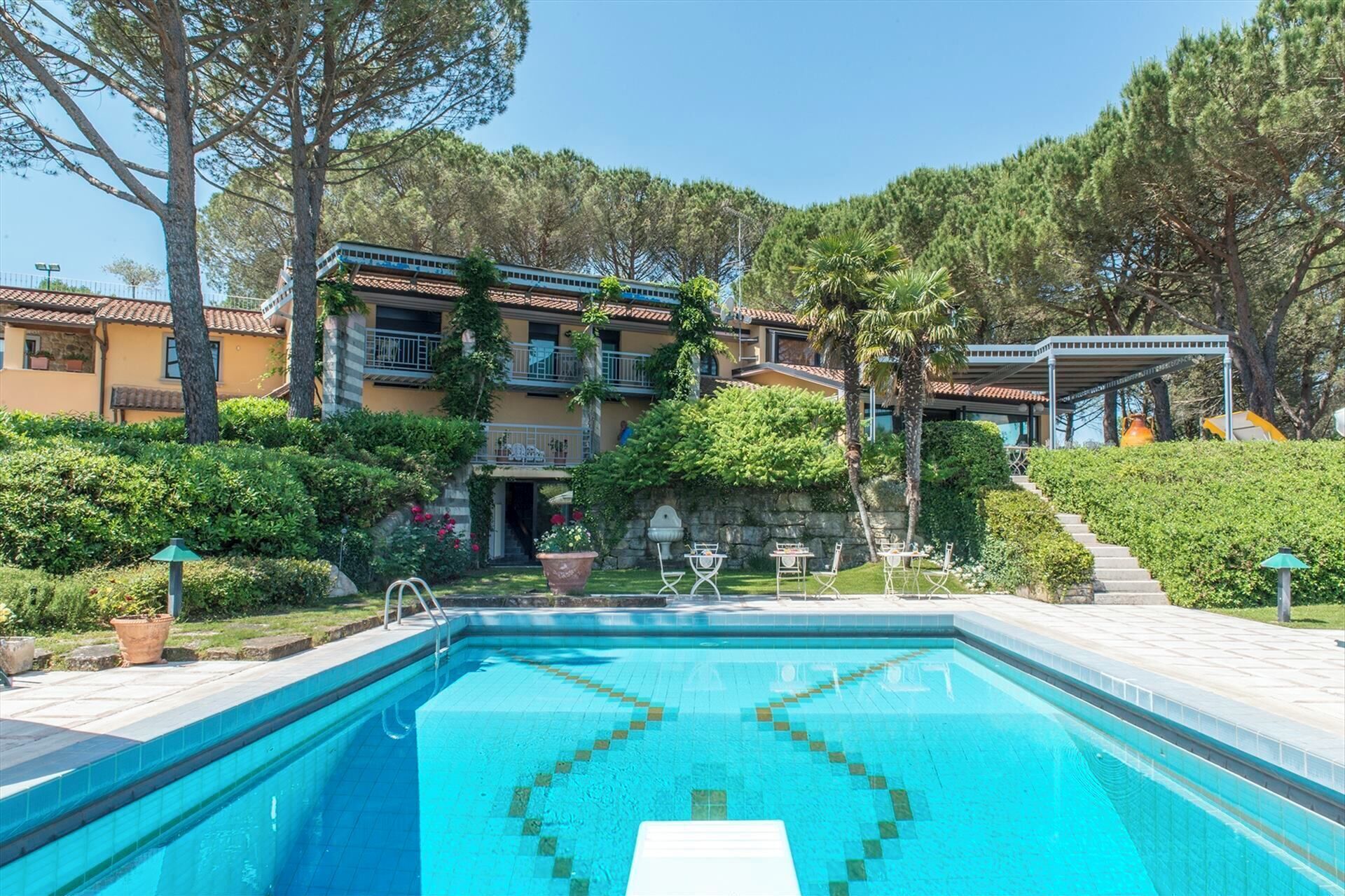 A swimming pool with a tiled deck, surrounded by a landscaped garden with various plants and trees.