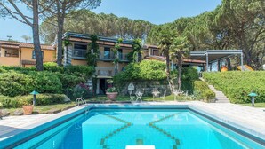 A swimming pool with a tiled deck, surrounded by a landscaped garden with various plants and trees.