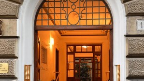 Imponente ingresso con arco in pietra, una scalinata che conduce a una porta e un cartello che indica il luogo.