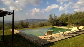 An infinity pool with lounge chairs, a pergola, and a view of distant hills. - Exceptionally pretty cottage with pool, views, in walking distance from Panzano (Greve in Chianti)