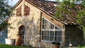 A stone building with a tiled roof, large windows, and potted plants. - Exceptionally pretty cottage with pool, views, in walking distance from Panzano (Greve in Chianti)