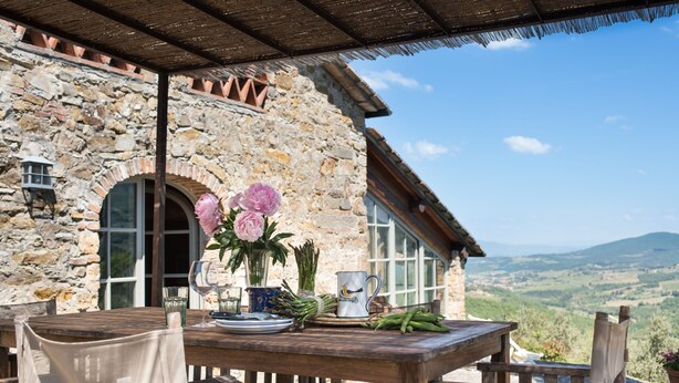 A rustic stone building with a wooden table set for dining, featuring a vase of flowers, a wine glass, and a pitcher. - Exceptionally pretty cottage with pool, views, in walking distance from Panzano (Greve in Chianti)