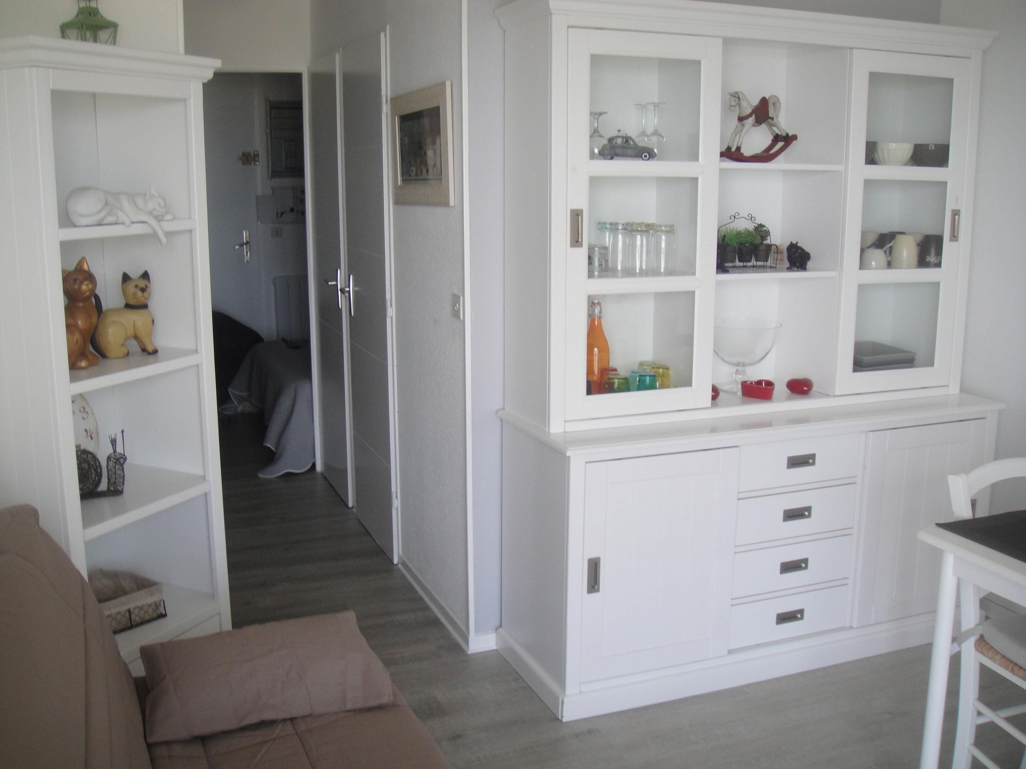 Un armario blanco con puertas de cristal que contiene cristalería y objetos decorativos.