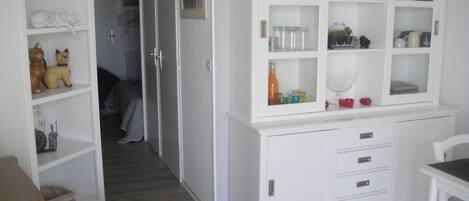 Un armario blanco con puertas de cristal que contiene cristalería y objetos decorativos.