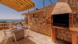 Een terras buiten, met een stenen muur, een barbecue en een eettafel.