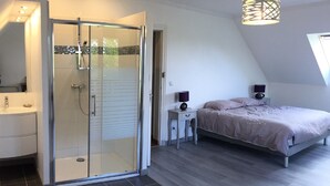 A bedroom with a bed, bedside tables, a nightstand, a glass-enclosed shower, a white sink, and a window. - Norman house with garden near the landing beaches  (Ver-Sur-Mer)