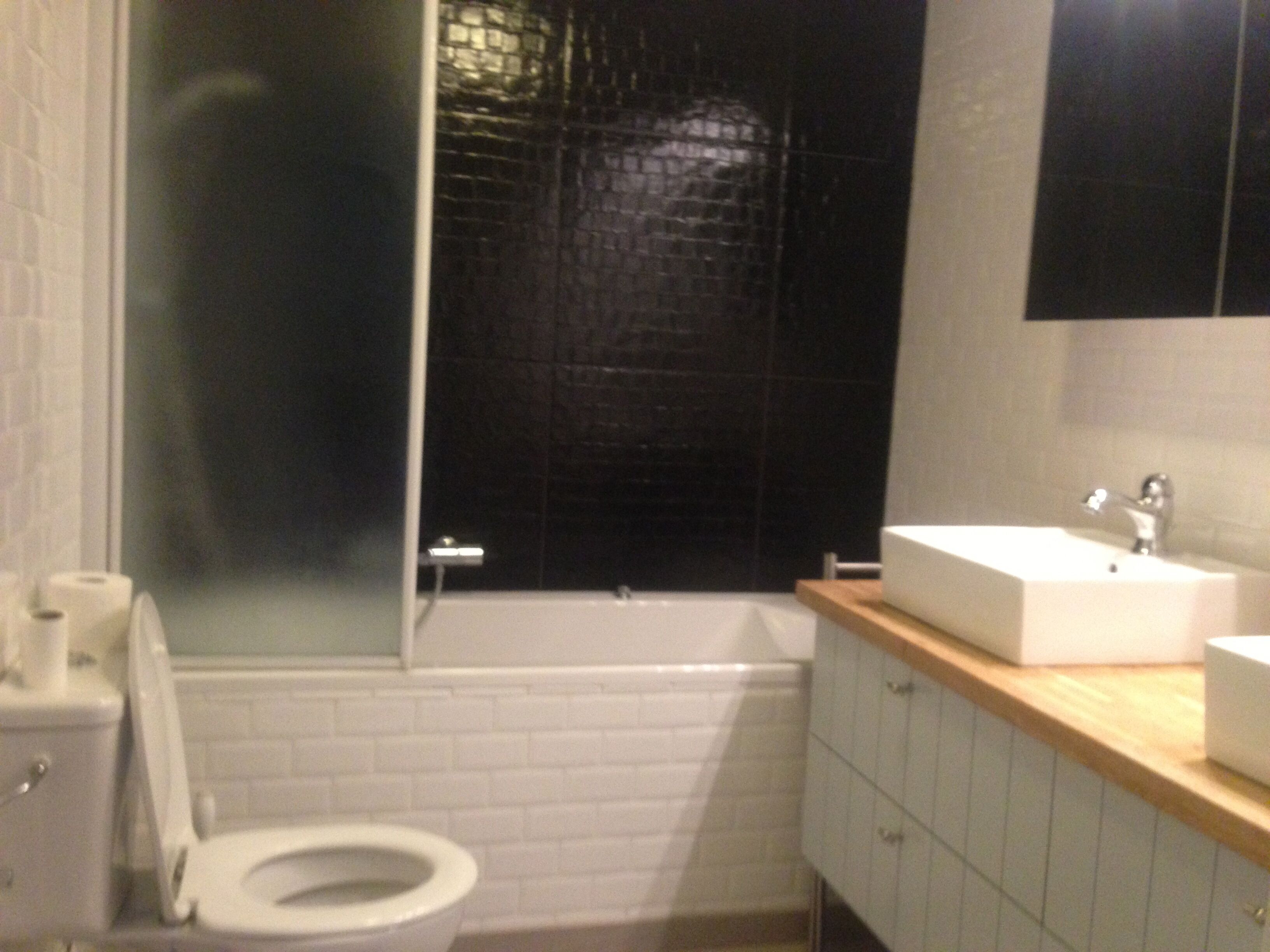 Une salle de bain avec des toilettes blanches, une baignoire et un lavabo posé sur un plan de travail en bois.