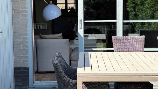 Une porte-fenêtre coulissante donne sur un espace de vie comprenant un canapé, des fauteuils en osier et une table.