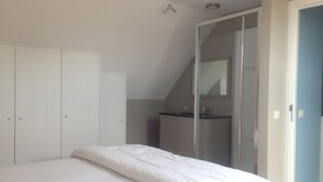 Une chambre avec un grand lit, une armoire, une salle de bain avec un miroir et un escalier.