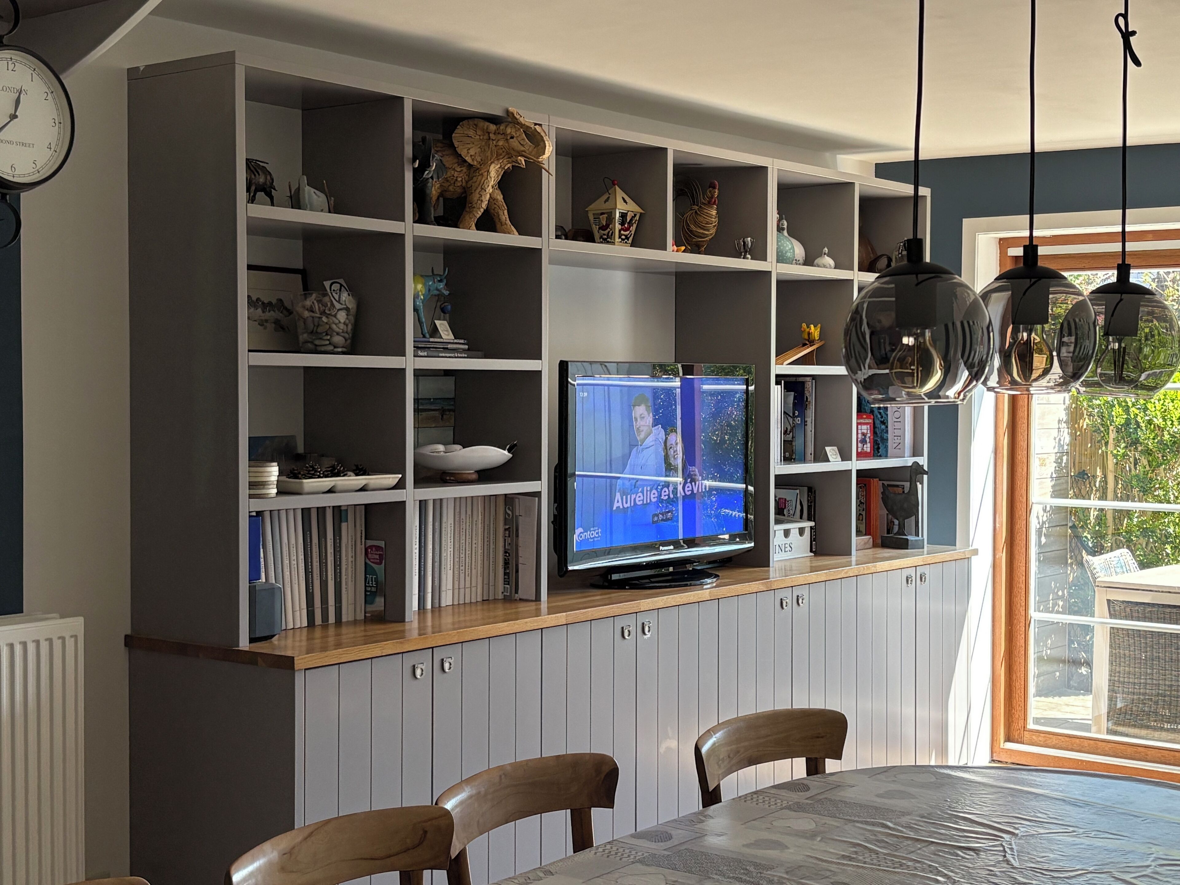 A modern living room with a TV, wooden dining table, and grey cabinets.
