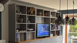 Un salon moderne avec un téléviseur, une table à manger en bois et des meubles de rangement gris.