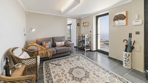 A modern living room with a grey sofa, wicker chairs, a patterned rug, and a view through a glass door. - Villa Clementina | Cliffs & Ocean | Heated Pool 26ºC (Prazeres)