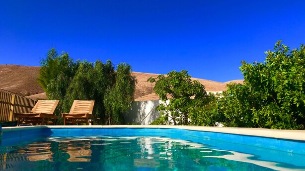 Ein klarer, blauer Swimmingpool mit Holzliegen und Blick auf einen Wasserfall.