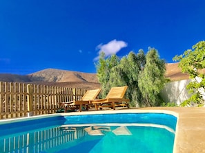 Une piscine avec deux chaises longues en bois, une clôture en bois et une vue sur les montagnes en arrière-plan.