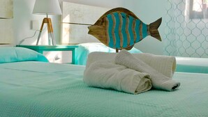Ein ordentlich bezogenes Bett mit einem gefalteten Handtuch, einer Holzfisch-Dekoration und einer Lampe auf einem Nachttisch.
