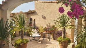 Un patio soleado con macetas de terracota, una silla de descanso y plantas en macetas.