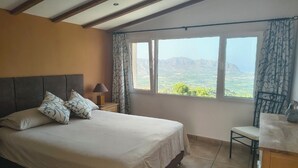 Un dormitorio con cama, una silla, un escritorio y un amplio ventanal con vistas a montañas.