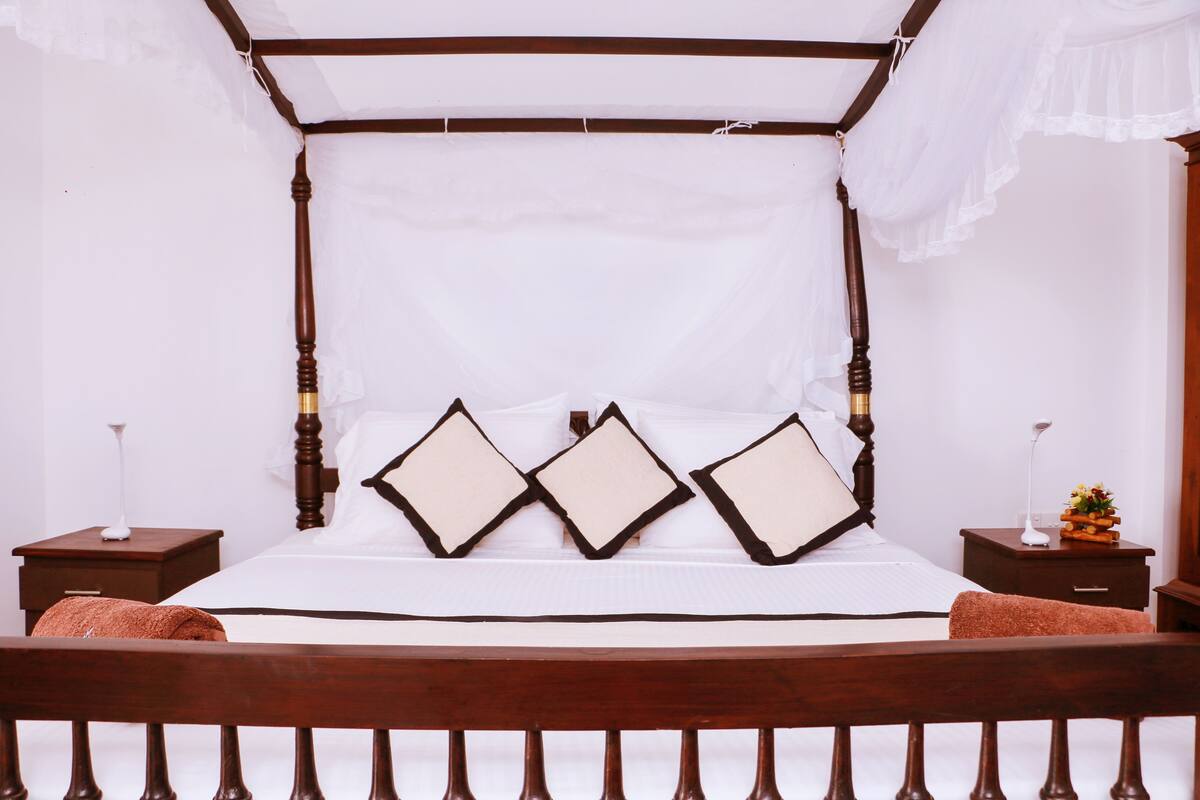 A four-poster bed with a canopy, white bedding, and three decorative pillows.