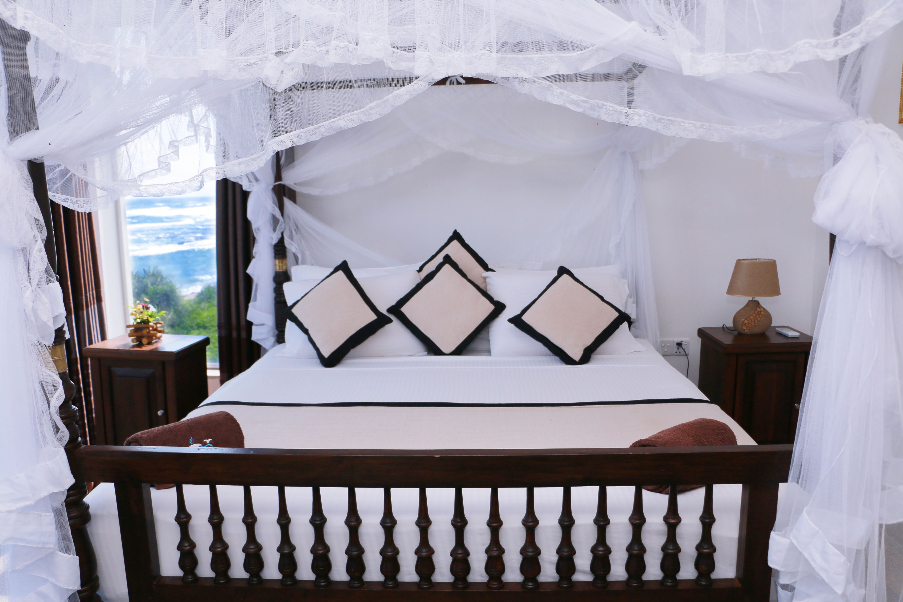 Una cama con dosel, almohadas y una mesita de noche con lámpara.