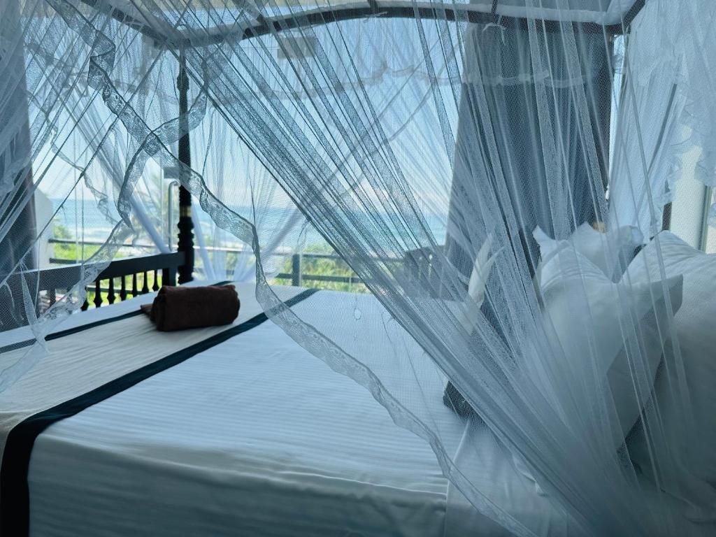 Una cama con sábana blanca, almohada marrón, mosquitero y vistas a la vegetación.