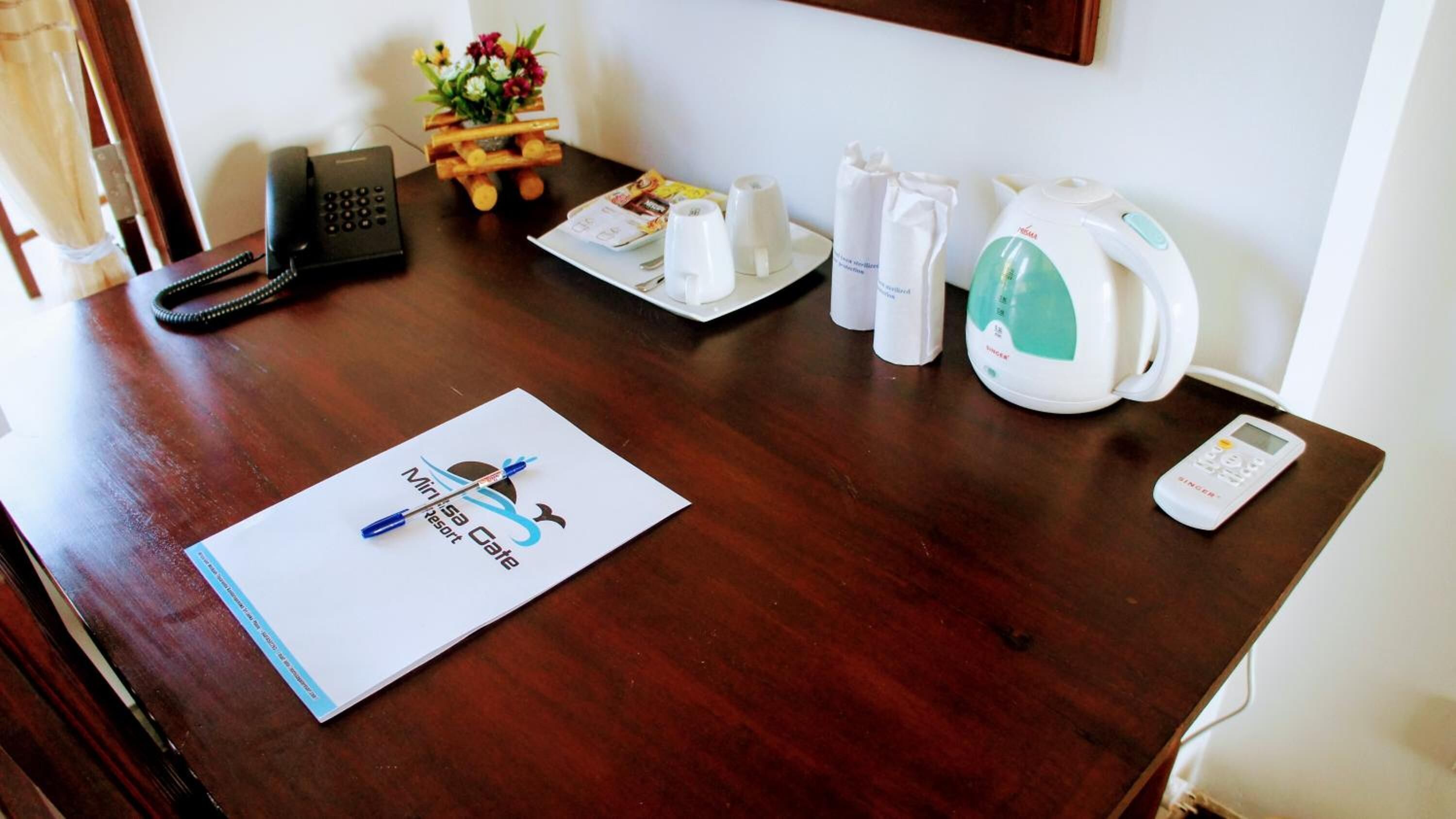 A wooden desk with a Minisa Cote brochure, a telephone, a small wooden stand with flowers, a kettle, and a cup.