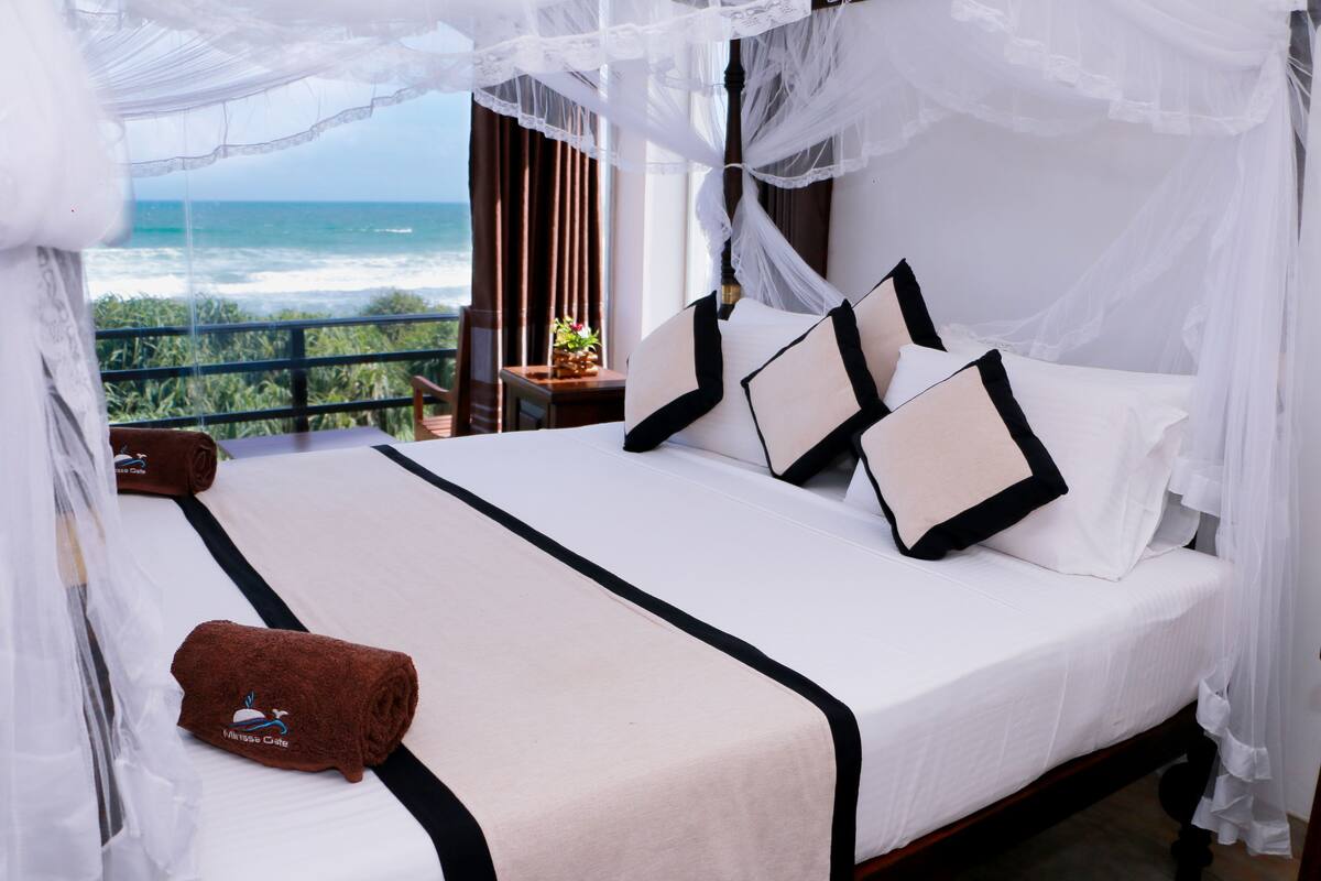 A bed with a canopy, white bedding, and a view of the ocean.
