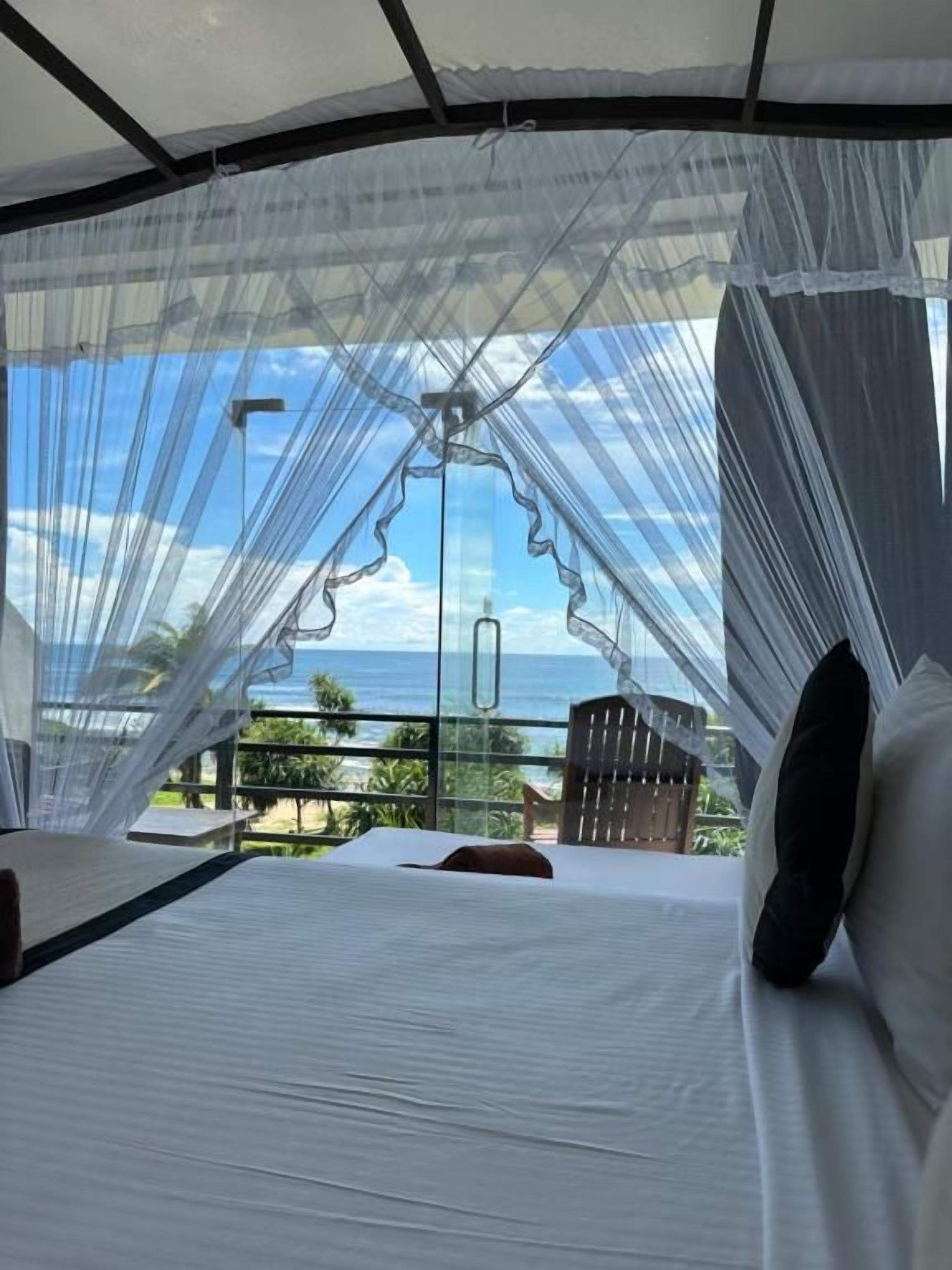 Una cama con vistas al océano a través de una cortina translúcida.