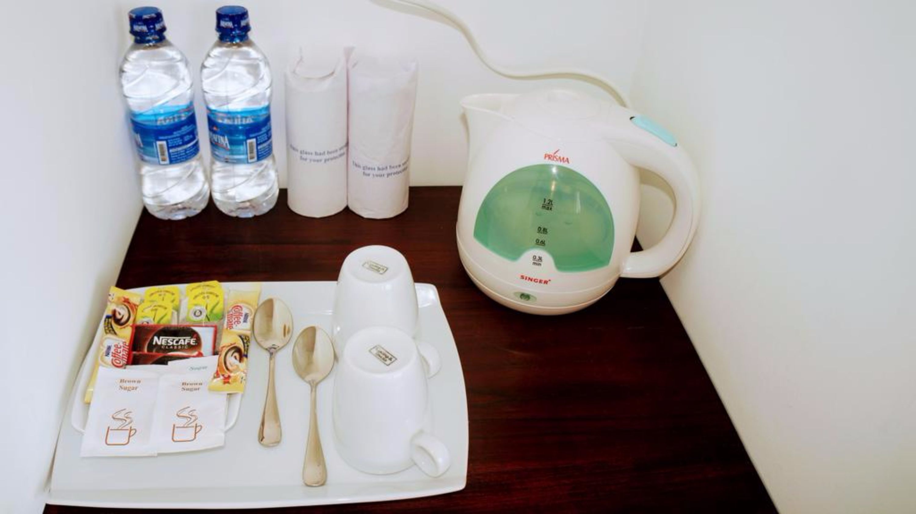 A breakfast setup with a kettle, water bottles, coffee packets, and sugar packets on a tray.