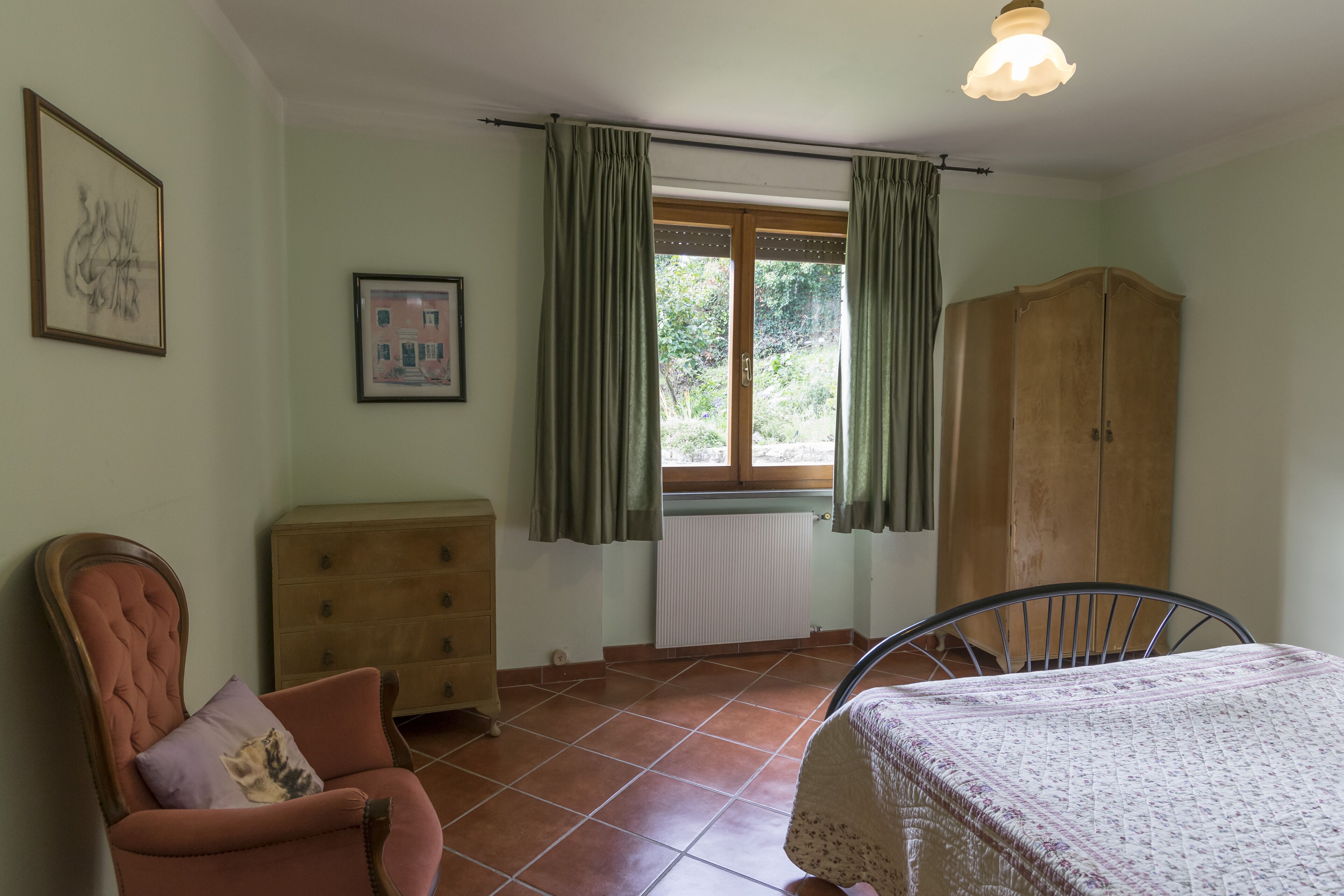 A room with a bed, a chair, a dresser, a wardrobe, and a window with curtains.