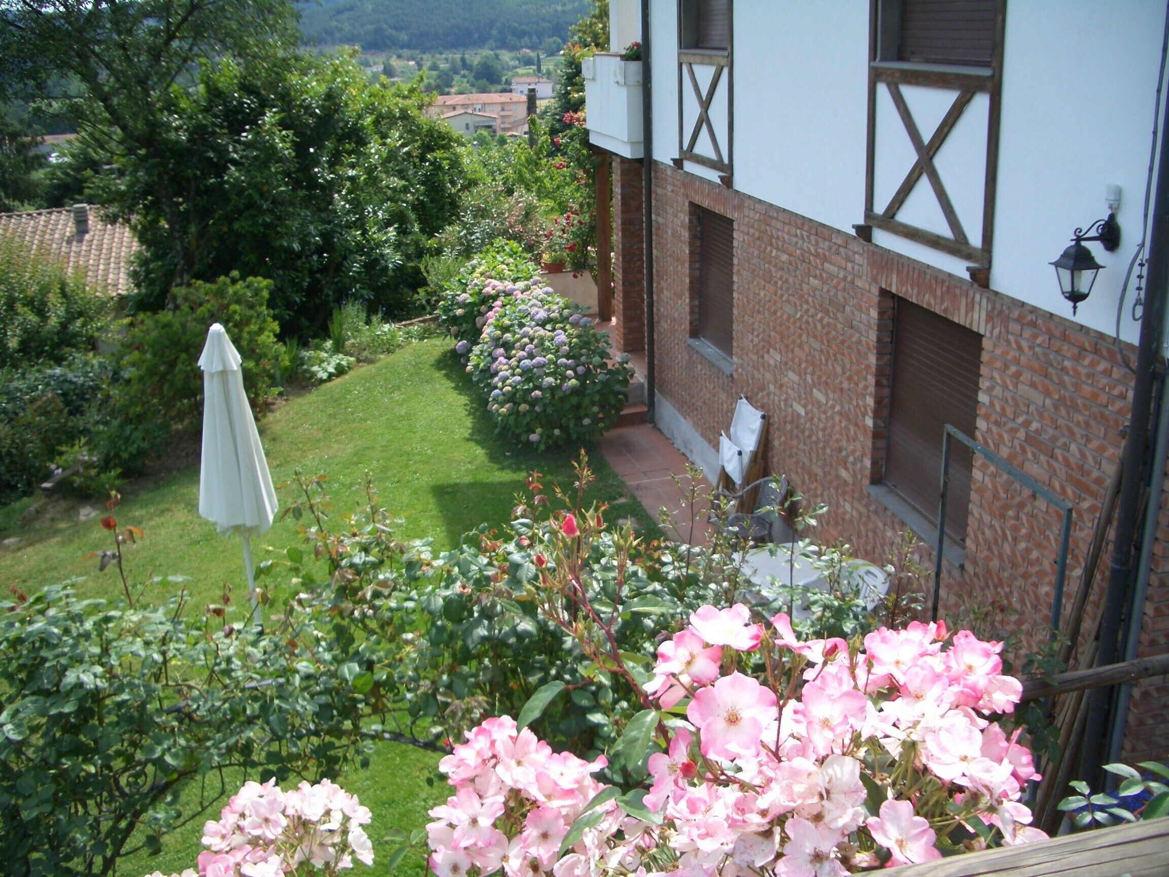 Ein Garten mit einem weißen Sonnenschirm, einer Backsteinmauer und Blick auf die Umgebung.