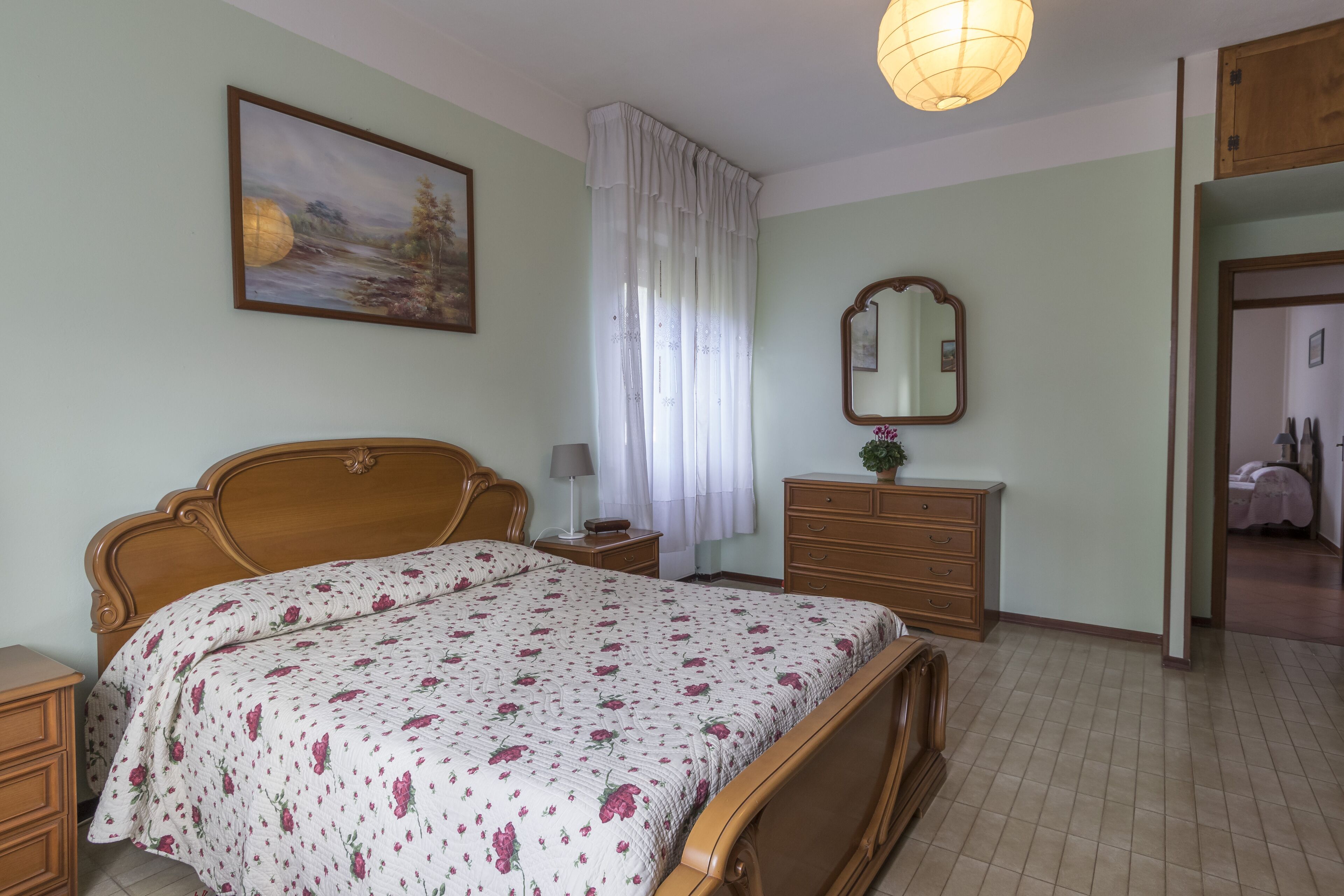 Ein Schlafzimmer mit einem Holzbett, einem Nachttisch, einer Kommode, einem Spiegel und einem Bild an der Wand.