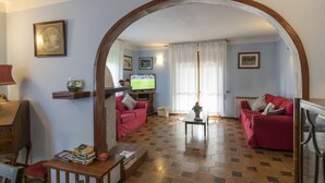 Een woonkamer met een rode bank, een houten salontafel en een televisie. Er is een boekenkast met boeken en een ingelijst schilderij aan de muur.