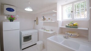 Een keuken met een fornuis, oven en wastafel. Er staan planken met potten en een mand met fruit.