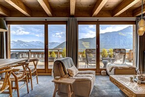 A cozy room with a large window, wooden furniture, and a view of mountains.