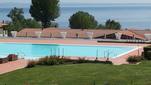 Un espace piscine offrant une vue dégagée sur la mer, entouré d’un toit en tuiles et de chaises longues blanches.
