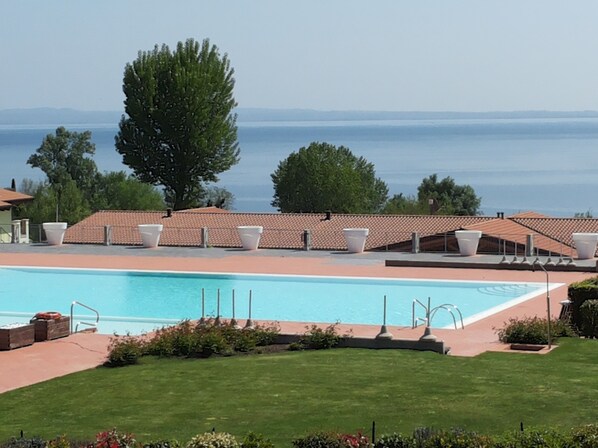 A pool area with a clear view of the sea, surrounded by a tiled roof and white lounge chairs.