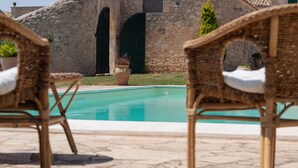 Un área junto a la piscina con sillas de mimbre y una pared de piedra al fondo.