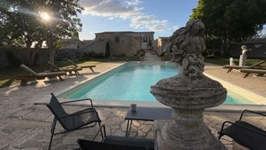 A pool area with stone chairs, a stone fountain, and a building in the background.