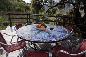 A round table with a mosaic top, surrounded by red wicker chairs, set on a terrace with a view of a mountainous landscape. - Villa Las Encinas on the Costa del Sol.        (Torrox)