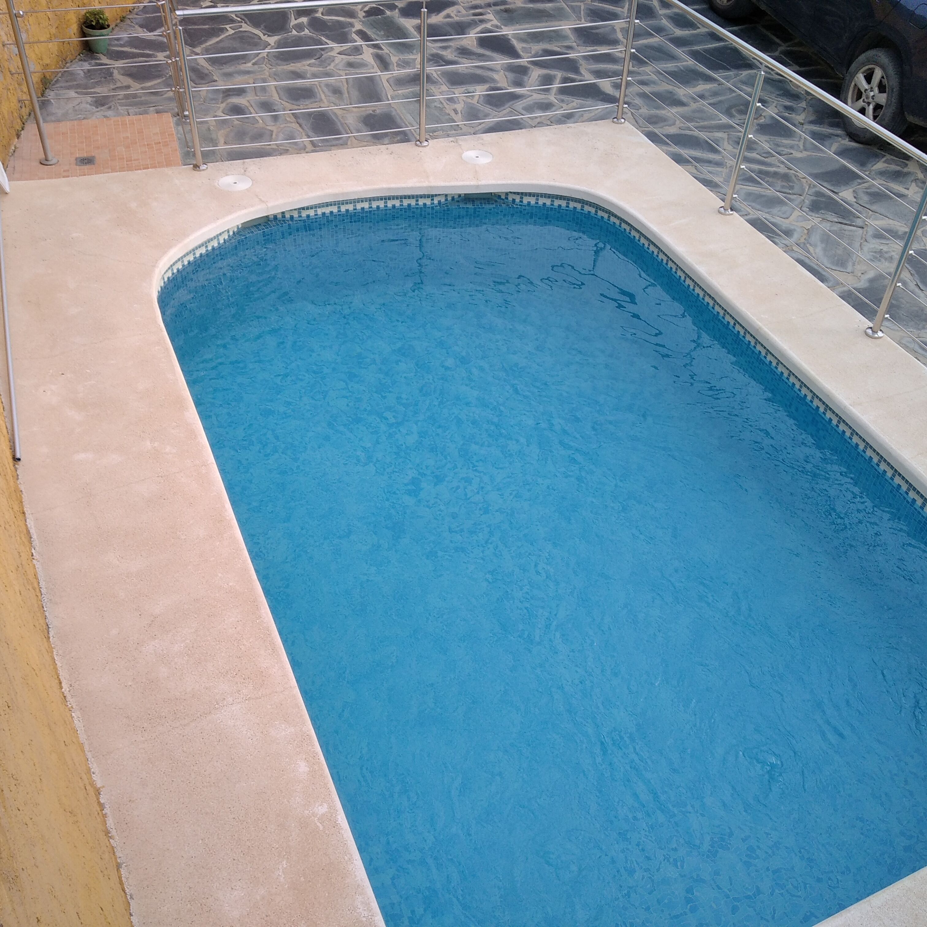 Une piscine rectangulaire avec un bord carrelé et une rambarde de sécurité en métal.