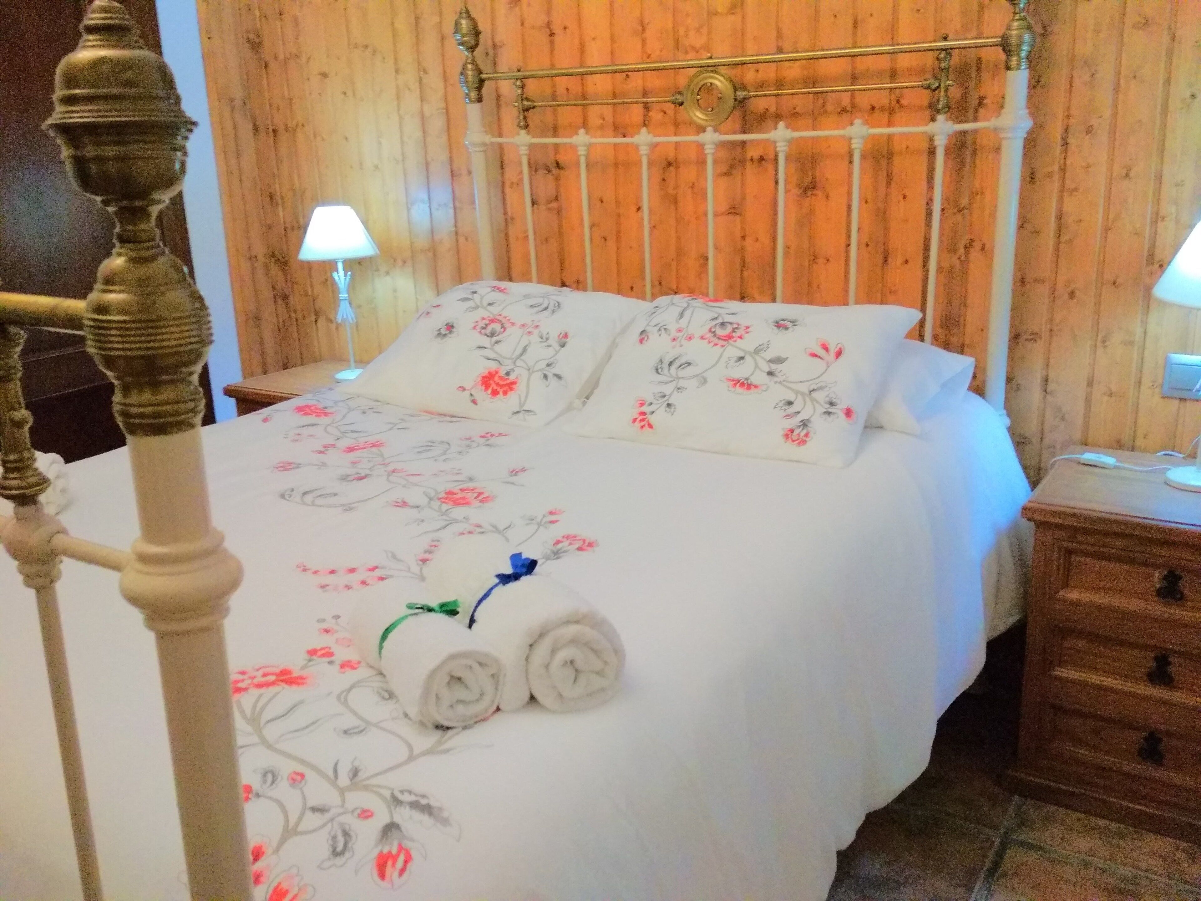 Un lit avec une literie à motifs floraux, deux lampes de chevet et une table de nuit en bois.