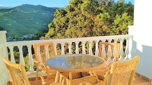 A wicker table and chairs on a balcony with a white railing, overlooking a green landscape with hills and trees. - Villa Las Encinas on the Costa del Sol.        (Torrox)