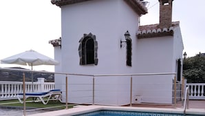 A swimming pool with a white building in the background, a white fence, and a white umbrella. - Villa Las Encinas on the Costa del Sol.        (Torrox)