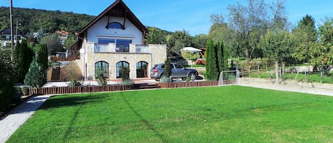 A two-story stone house with a balcony, a driveway, and a well-maintained lawn.